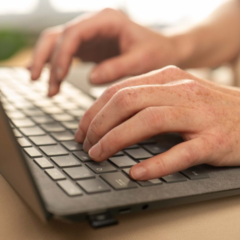 Hände tippen auf einer dunklen Tastatur, im Hintergrund unscharf.